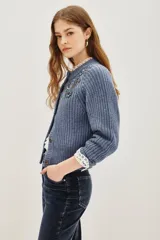 Cardigan de punto acanalado color azul grisáceo, de corte cropped y abotonadura frontal. Presenta apliques florales bordados con cuentas y lentejuelas en tonos azules y verdes en la parte delantera.