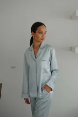 Pijama de satén elastizado color celeste, compuesto por una camisa de manga larga con cuello solapa, botones frontales y bolsillo en el pecho, y un pantalón recto con cintura elástica y lazo ajustable.