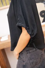 Blusa negra de corte holgado con mangas cortas tipo murciélago y cuello redondo. Confeccionada en tela con textura sutil.