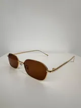 Lentes de sol con armazón metálico dorado y cristales oscuros de forma rectangular con bordes redondeados. Cuentan con protección UV400.
