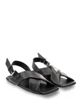 Sandalias bajas color blanco hueso, con punta cuadrada, tiras anchas cruzadas en el empeine y ajuste con hebilla en el tobillo.