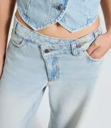 Pantalón wide leg de tiro medio confeccionado en denim de algodón. Presenta un diseño de cintura cruzada con cierre tradicional, trabillas para cinturón y bolsillos funcionales.