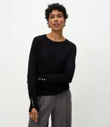 Suéter de punto negro de corte ajustado y manga larga, con cuello redondo y detalles de botones metalizados dorados en los puños. Marca Cortelle.