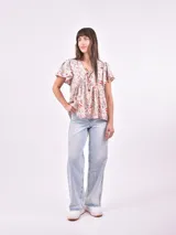 Blusa estampada con cuello en V y lazo ajustable en el escote. Presenta mangas cortas con ligero volumen y un corte holgado con frunces bajo el busto.