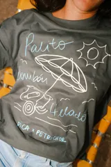 Remera oversize color gris oscuro con estampa frontal en tonos claros que incluye un carrito de helados, una sombrilla y el texto 'Palito Bombón Helado' junto a la firma de la colaboración Pica x Petrichor.