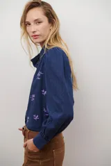 Camisa blanca de manga corta con cuello mao y volados, botones frontales y bordados de hojas y flores en color dorado.