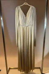 Vestido largo de fiesta en color negro con acabado brillante. Presenta un escote en V, cintura entallada con detalle de cinturón fino y mangas largas tipo capa con efecto plisado.