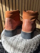 Botas Saura de cuero y gamuza en color tostado, con cordones frontales, suela gruesa y diseño tipo borceguí.