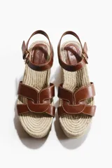 Sandalias de tacón corrido con plataforma de yute trenzado, tiras de cuero marrón en el empeine y tira ajustable con hebilla en el tobillo.