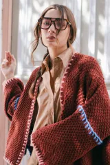 Saco oversize de tejido de punto en color beige, con mangas caídas y detalles de bordado a mano en tonos verde y lila en los bordes y costuras.