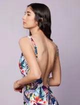 Malla enteriza con escote en V cruzado y breteles finos regulables, confeccionada en tejido estampado con diseño tropical y floral en tonos blancos, fucsias, azules y verdes.