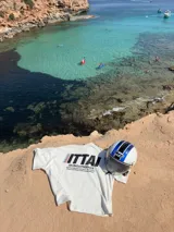 Remera marrón de corte holgado con estampado en la espalda que incluye la palabra "ITTAI" en blanco con líneas rojas y azules, la frase "AN IBIZA PRODUCE" y un texto más pequeño que dice "Ittai Stars Department Gallery - Ibiza Edition. If you're in Ibiza, 112 is not an option.".