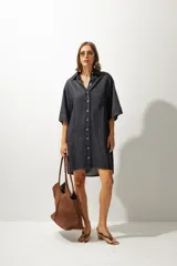 Vestido camisero corto de denim color gris oscuro, con mangas cortas, cuello camisero, cierre frontal de botones y un bolsillo aplicado en el pecho.
