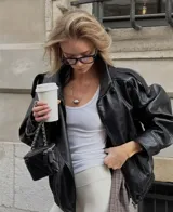 Chaqueta de cuero sintético color negro con acabado granulado, diseño oversize, cuello alto estructurado y cierre asimétrico.