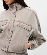 Campera bomber color gris de sarga, con cuello alto, cierre frontal con botones y bolsillos con solapa en el pecho. Presenta mangas largas con puños elásticos y ruedo ajustable con elástico.