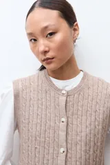 Chaleco de punto con textura acanalada, color tostado melange, con cuello redondo y cierre frontal de botones.