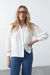 Camisa de manga larga en color celeste, con diseño de corte relajado, cuello clásico y detalle de tablas verticales en el frente.