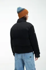 Campera negra de estilo urbano, confeccionada en una combinación de tela técnica y textura tipo corderito (fleece). Presenta cierre frontal con solapa y botones a presión, cuello alto y logo estampado en el pecho.