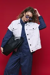 Chaleco de jean color blanco, de corte oversized, con cuello camisero, bolsillos delanteros con solapa y cierre frontal por botones metálicos.