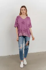 Blusa lila de algodón con escote en V, mangas cortas y holgadas. Presenta estrellas bordadas en relieve en la parte superior y un borde de lentejuelas en el dobladillo inferior.
