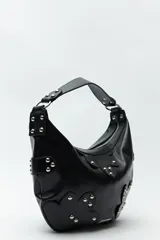 Cartera marrón de cuero sintético con forma de media luna, asa corta y apliques de tachas metálicas plateadas.