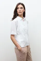 Camisa blanca de manga corta con sutiles detalles bordados tonales, cierre frontal de botones y cuello camisero.