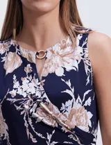 Vestido largo de seda fría con estampado floral en tonos beige y blanco sobre fondo azul marino. Tiene cuello redondo cruzado con abertura y aplique metálico.