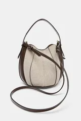 Bolso tipo saca con diseño estructurado, confeccionado en una combinación de tejido de lana en tono beige y laterales de cuero sintético marrón. Presenta costuras decorativas verticales, asa de mano superior y una correa bandolera extraíble con detalle de franjas. Cuenta con cierre mediante botón imantado.