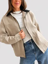 Campera de gabardina color marrón con cierre frontal y cuello en contraste color negro. Presenta bolsillos delanteros funcionales y diseño de corte recto.