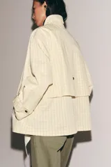 Chaqueta de corte recto confeccionada en algodón con estampado de cuadros. Presenta cuello solapa en color azul marino a contraste, cierre frontal con botones ocultos bajo solapa, bolsillos laterales y mangas largas con trabillas ajustables en los puños.