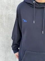 Canguro negro con capucha ajustable con cordones, bolsillo tipo canguro y logo bordado en azul en el pecho.