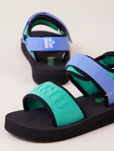 Sandalias negras de estilo deportivo con plataforma gruesa de EVA. Presentan tiras ajustables con velcro, una tira frontal ancha con relieve de la palabra "RUSTY" y una tira trasera para el talón.