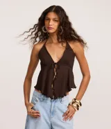 Blusa beige texturizada de corte halter con escote en V, lazo frontal ajustable en el busto y ruedo asimétrico ondulado.