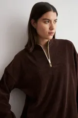 Sweater de tejido acanalado color marrón, con cuello alto y cierre frontal parcial. Presenta un diseño holgado de manga larga con hombros caídos.