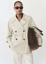 Anorak color beige con cuello de solapa, doble botonadura, manga larga con trabillas y dos bolsillos laterales. Diseño recto y midi con forro interior.