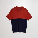 Remera de punto de manga corta con cuello polo, diseño bicolor que combina un tono rojizo en la parte superior y azul marino en la parte inferior.