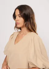 Vestido corto color beige, de corte oversize, con escote en V y mangas globo. Incluye cinturón marrón con hebilla dorada.