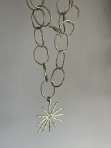 Collar plateado con cadena de eslabones ovalados y dije en forma de sol con centro negro.