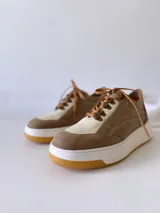 Championes de cuero color visón con cordones marrones, suela blanca y base color caramelo.