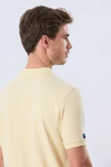 Remera polo piqué de algodón color amarillo, con cuello y puños acanalados, y cierre frontal de botones.