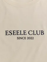 Remera oversize de color arena, 100% algodón, con estampa en la espalda que ilustra el puente de La Barra durante el atardecer, acompañada de texto descriptivo y de la marca Eseele Club.