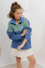 Buzo verde con cierre metálico, cuello alto y bordados.