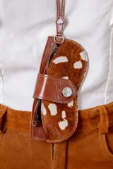 Accesorio porta lentes de cuero vacuno con diseño de pelo con manchas tipo animal print. Cuenta con una correa larga para colgar al cuello y un cierre frontal con broche metálico.