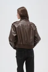 Campera de eco-cuero negro con cuello alto, cierre frontal, bolsillos con solapa en el pecho y puños y ruedo elásticos.