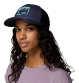 Gorro tipo trucker con paneles traseros de malla para mayor ventilación y cierre trasero ajustable a presión. Presenta un parche frontal con diseño de montañas y el logo de la marca.