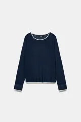 Jersey de punto efecto doble, color azul marino con detalles en blanco en el cuello, puños y ruedo. Presenta cuello redondo y manga larga con diseño de hombros raglán.