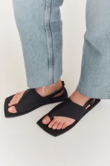Sandalias de cuero negro con diseño de punta cuadrada, tira ancha sobre el empeine y ajuste con correa en el talón.
