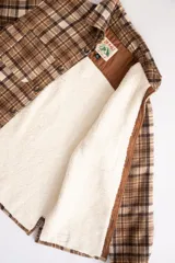Camisa leñadora marrón a cuadros con forro de corderito sintético, cierre con botones y dos bolsillos frontales con tapa.