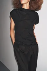 Top negro de manga corta y cuello subido, con detalle de nudos y frunces distribuidos en el frente y laterales, creando textura.