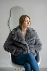 Abrigo corto de piel sintética en color gris, con solapas anchas y mangas largas. Diseño de corte recto y textura suave.